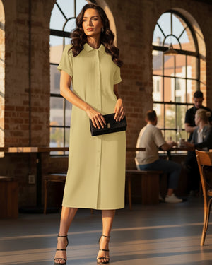 Woman in a light green dress holding a black clutch in an indoor setting with people in the background.