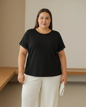 Woman wearing a black t-shirt with white polka dots and white pants in a minimal indoor setting.