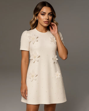 Woman wearing a white dress with floral embellishments against a gray background