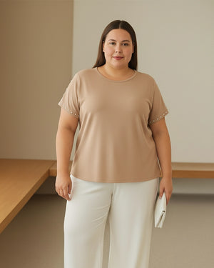 Woman wearing a beige top with white pants in a minimalistic setting