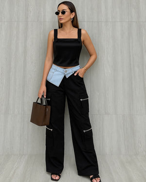 Woman wearing a black outfit with a light blue denim jacket, holding a brown handbag against a gray wall.