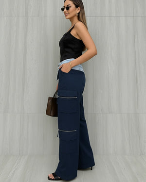 Woman wearing a black top and navy cargo pants against a light gray wall.