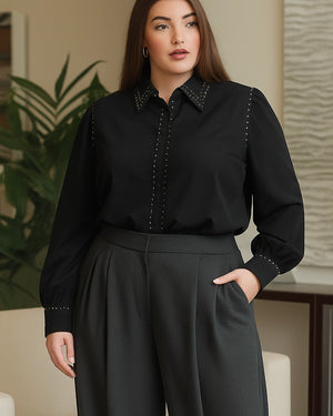 Woman wearing a black blouse with decorative elements and dark pants indoors.