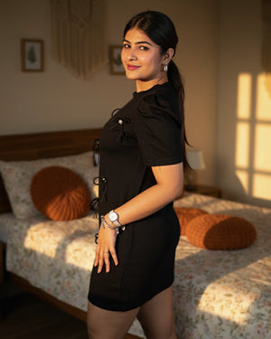 Woman in a black dress standing in a bedroom with sunlight streaming in