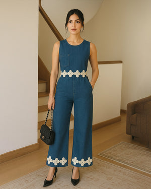 Woman wearing a blue jumpsuit with white floral details in an indoor setting.