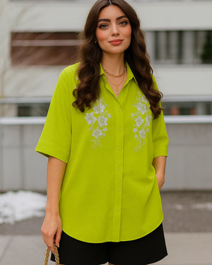 Woman wearing a bright green shirt with floral embroidery outdoors