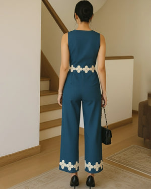Woman wearing a blue jumpsuit with white floral details in an indoor setting.