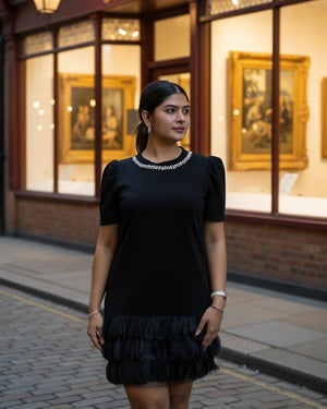 Woman in a black dress standing in front of a building with large windows displaying framed pictures.