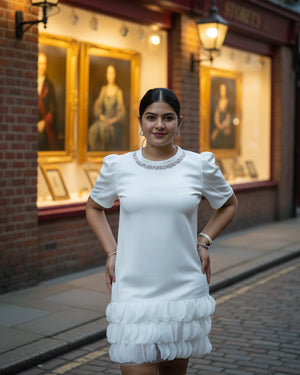 Woman in a white dress standing on a street with a building featuring portraits in the background