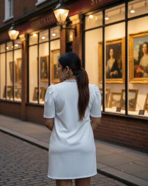 Woman in a white dress standing on a street looking at art in a gallery window.