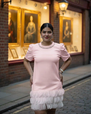 Woman in a pink dress standing in front of a building with portraits on the wall.