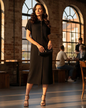 Woman in a black dress standing in a cafe with large windows.