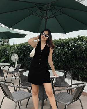 Woman in a black dress standing under a green umbrella in an outdoor setting.