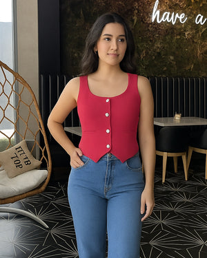 Woman wearing a red sleeveless top with buttons and blue jeans in an indoor setting.