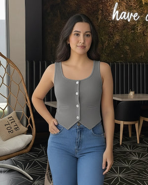 Woman wearing a gray tank top with buttons and blue jeans in an indoor setting.