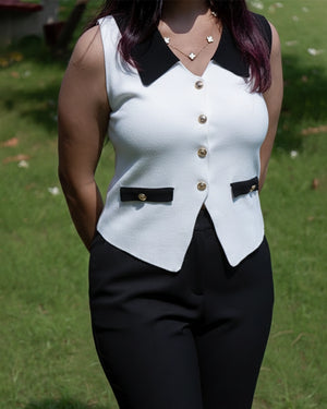 Person wearing a white sleeveless top with black accents and gold buttons, standing outdoors on grass.