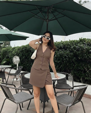 Woman in a brown dress standing under a large green umbrella in an outdoor setting.