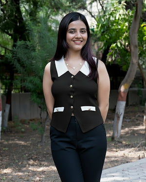 Woman wearing a black vest over a white shirt with a garden background