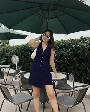 Woman in a navy blue dress standing under a green umbrella in an outdoor setting.