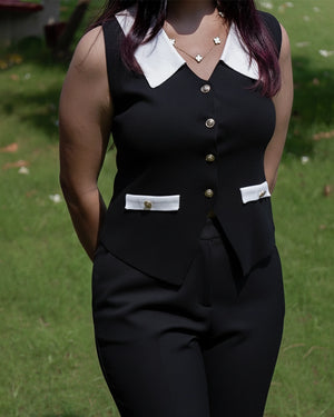 Person wearing a black sleeveless top with white collar and buttons, standing outdoors on grass.