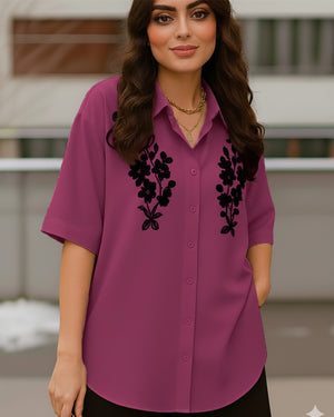Woman wearing a purple blouse with black floral embroidery outdoors.