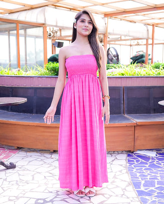 Woman in a pink dress standing in an outdoor setting with plants and tables.