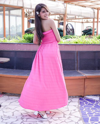 Woman in a pink dress standing outdoors with greenery in the background
