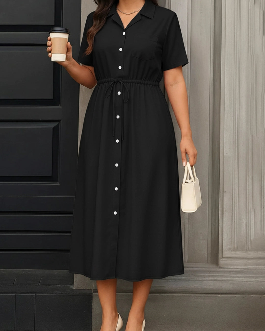 Woman wearing a black dress with white buttons, holding a coffee cup and a small white handbag.