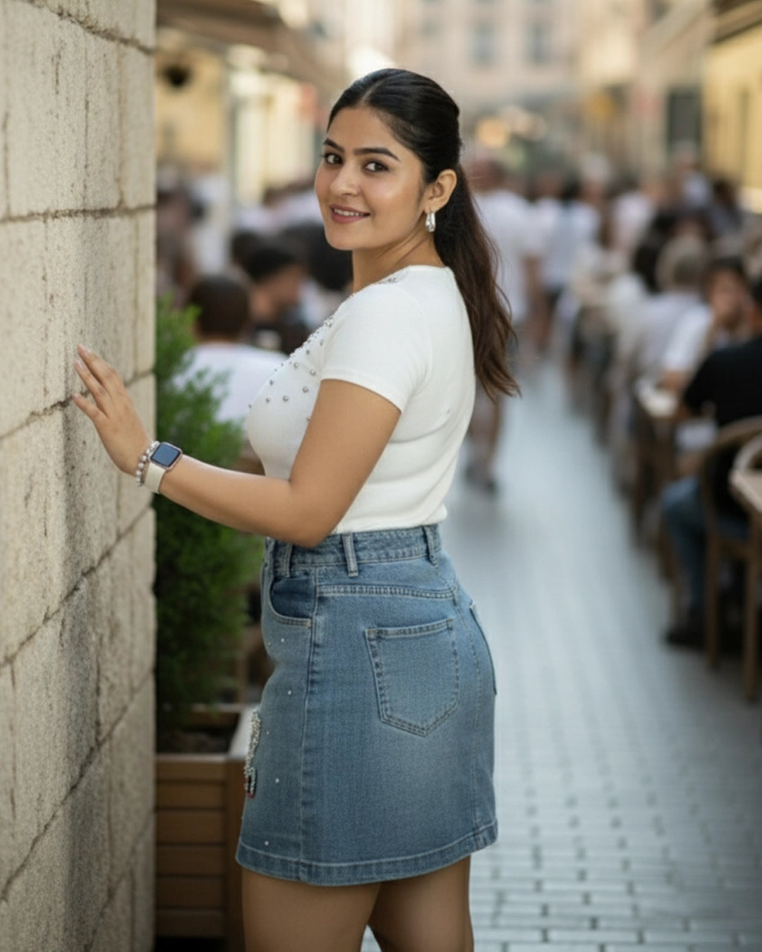 Woman in a white top and blue denim skirt standing against a stone wall in an urban setting.