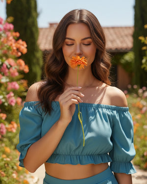 Woman in a blue top smelling a flower in a garden