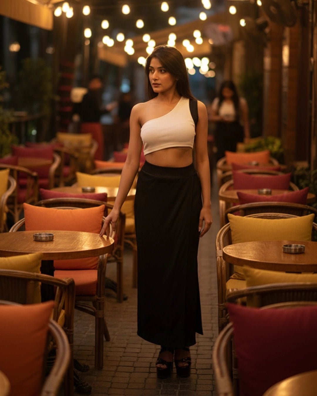 Woman in a white top and black skirt standing in a dimly lit cafe with string lights.