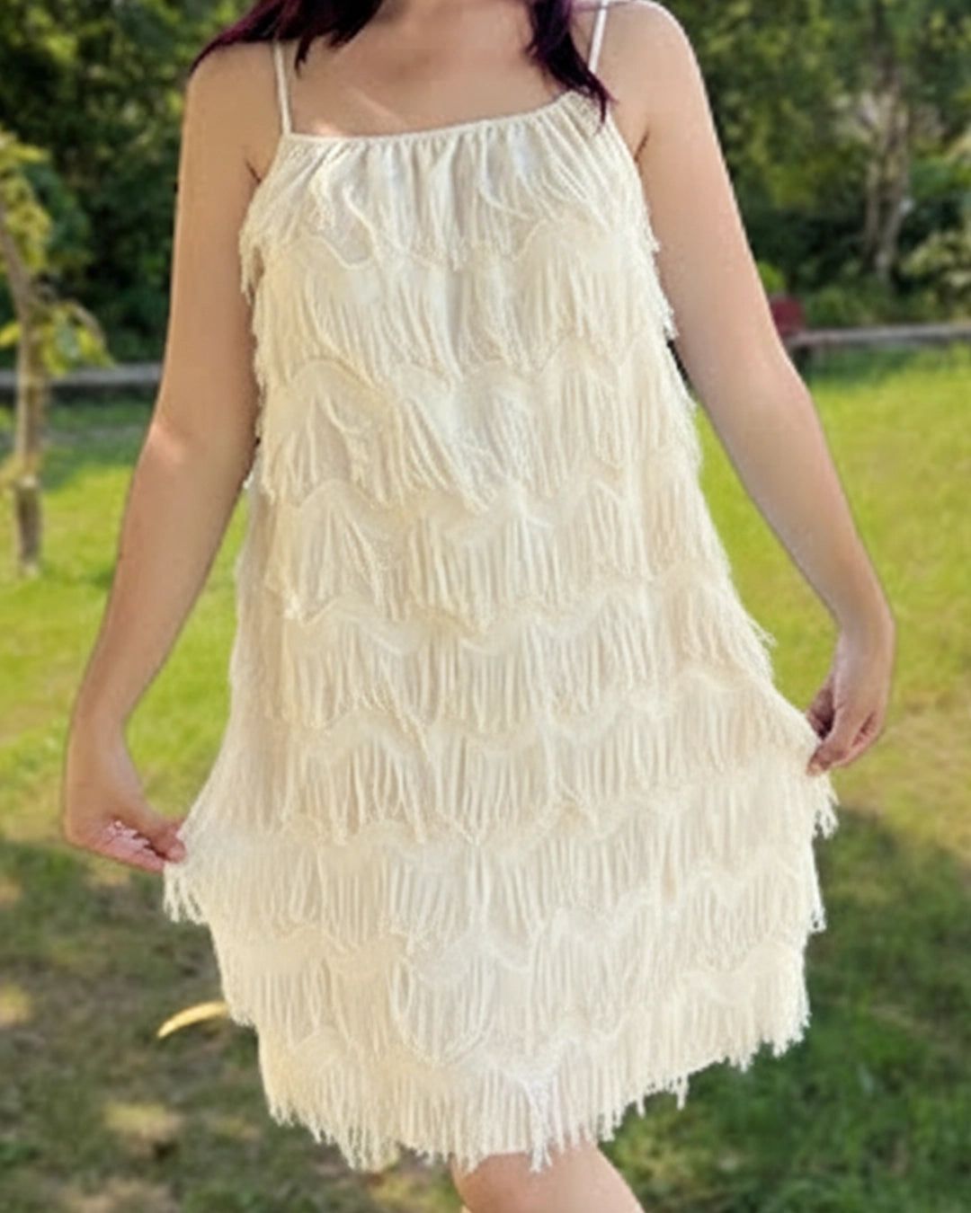 Woman wearing a white lace dress standing outdoors with greenery in the background