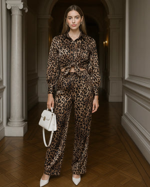 Woman in leopard print outfit holding a white handbag in an elegant hallway.