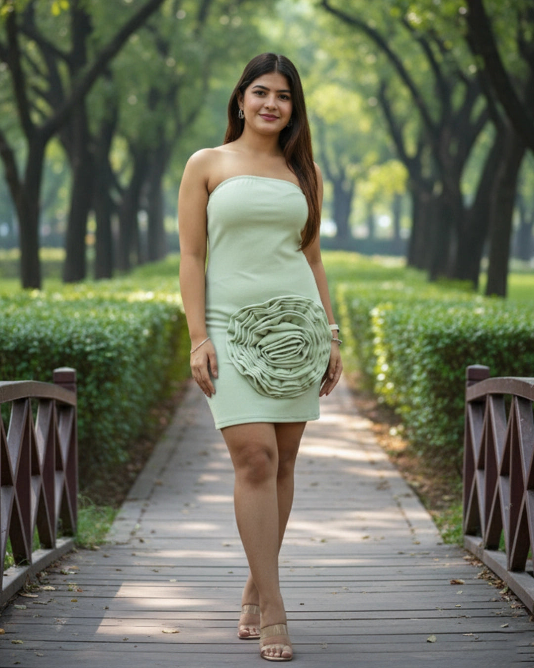 Woman in a light green strapless dress with floral details walking on a wooden path in a park.