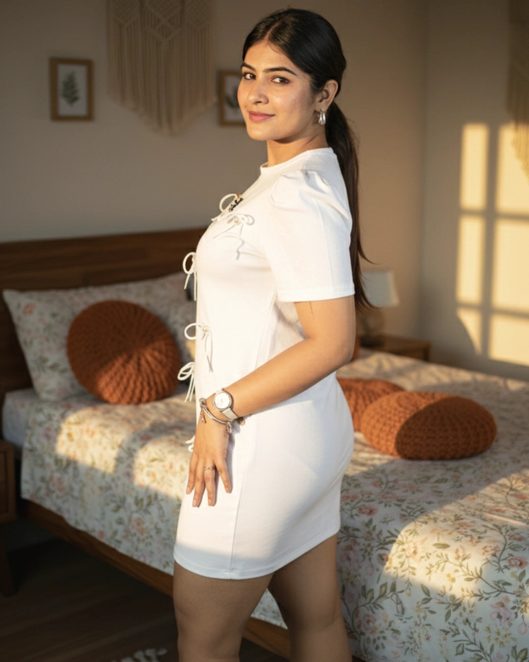 Woman in a white dress standing in a bedroom with floral bedding and wooden headboard.