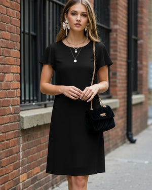 Woman wearing a black dress with a black handbag against a brick wall.