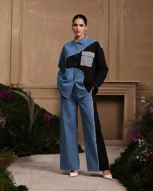 Woman wearing a black and blue outfit with a textured wall and plants in the background