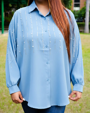 Person wearing a light blue blouse with decorative elements outdoors.