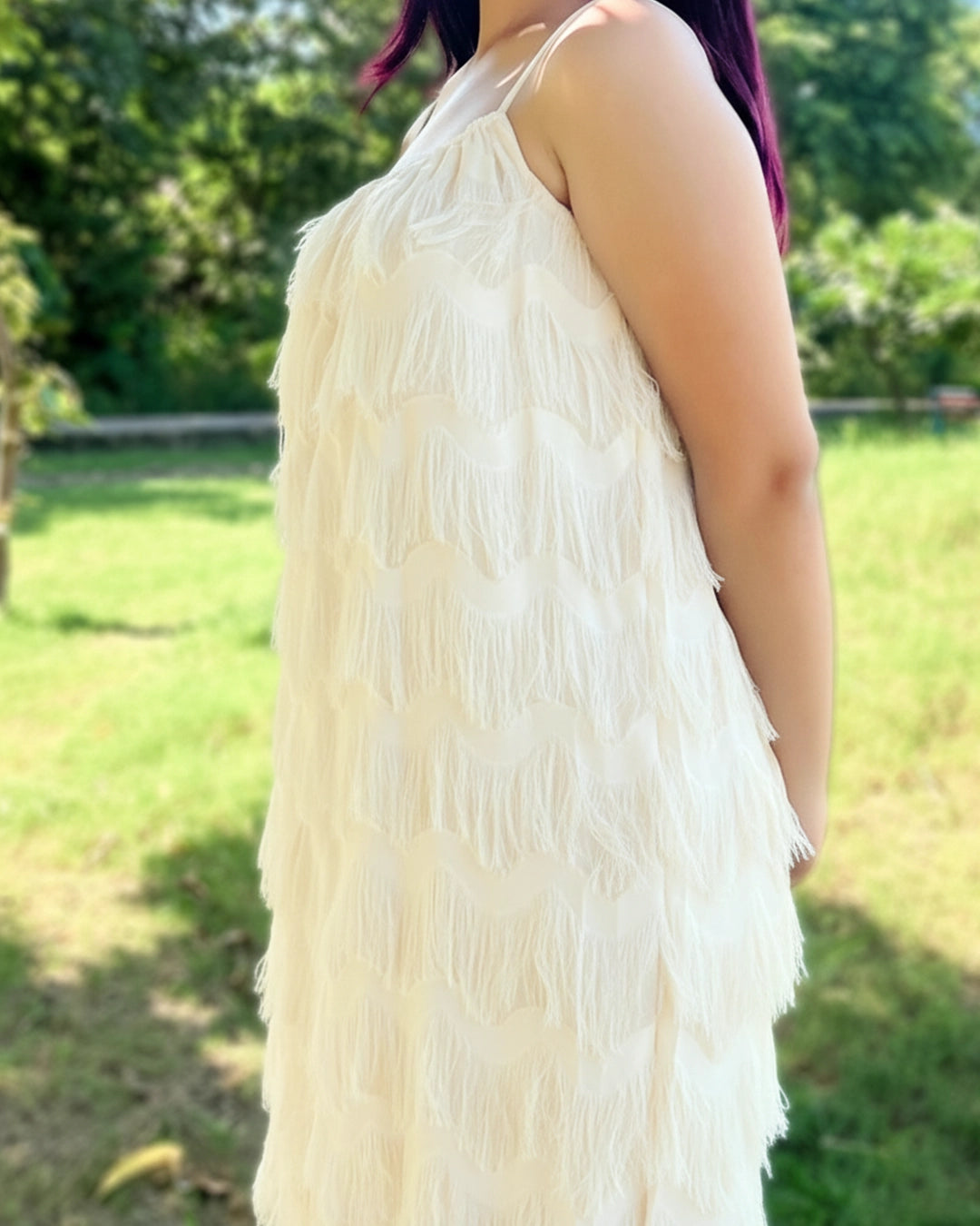 Person wearing a white fringe dress standing in a grassy outdoor area.