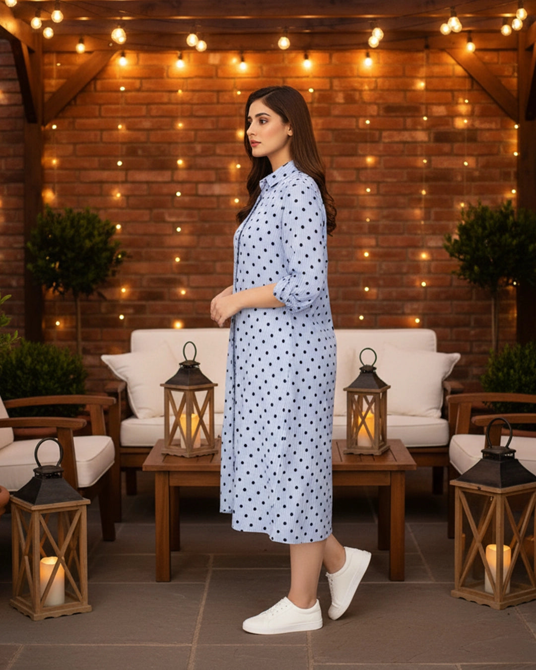 Woman in a polka dot dress standing in an outdoor setting with string lights and lanterns.
