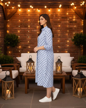 Woman in a polka dot dress standing in an outdoor setting with string lights and lanterns.
