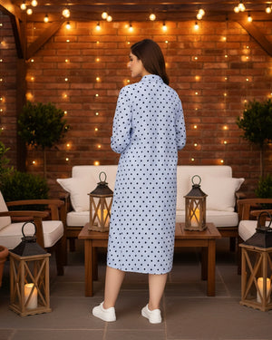 Woman in a polka dot robe standing in an outdoor setting with string lights and lanterns.