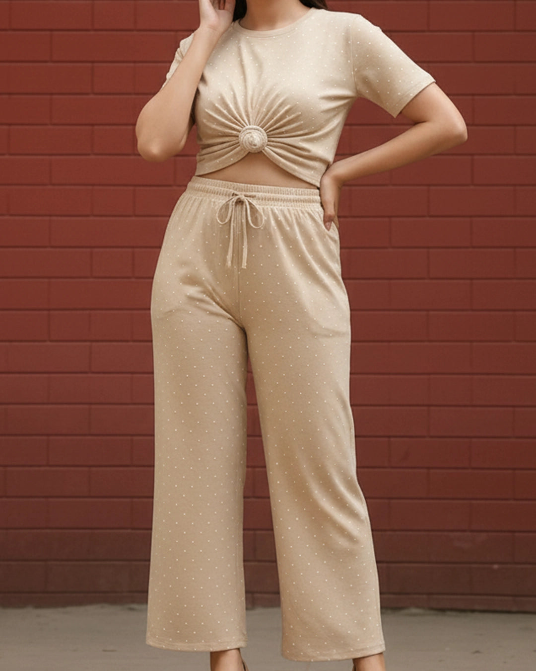 Person wearing a beige top and pants set against a red brick wall.