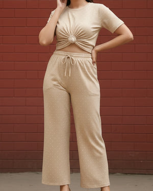 Person wearing a beige top and pants set against a red brick wall.