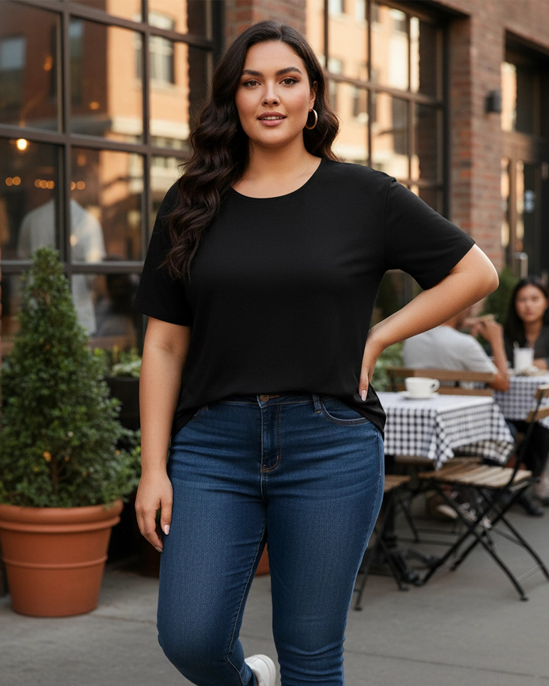 Woman wearing a black t-shirt and blue jeans standing outdoors with a blurred background