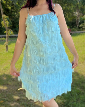 Woman wearing a light blue dress with ruffled layers outdoors.