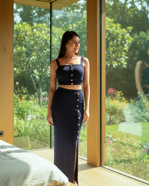 Woman in a navy blue outfit standing in a room with large windows showing a garden view.