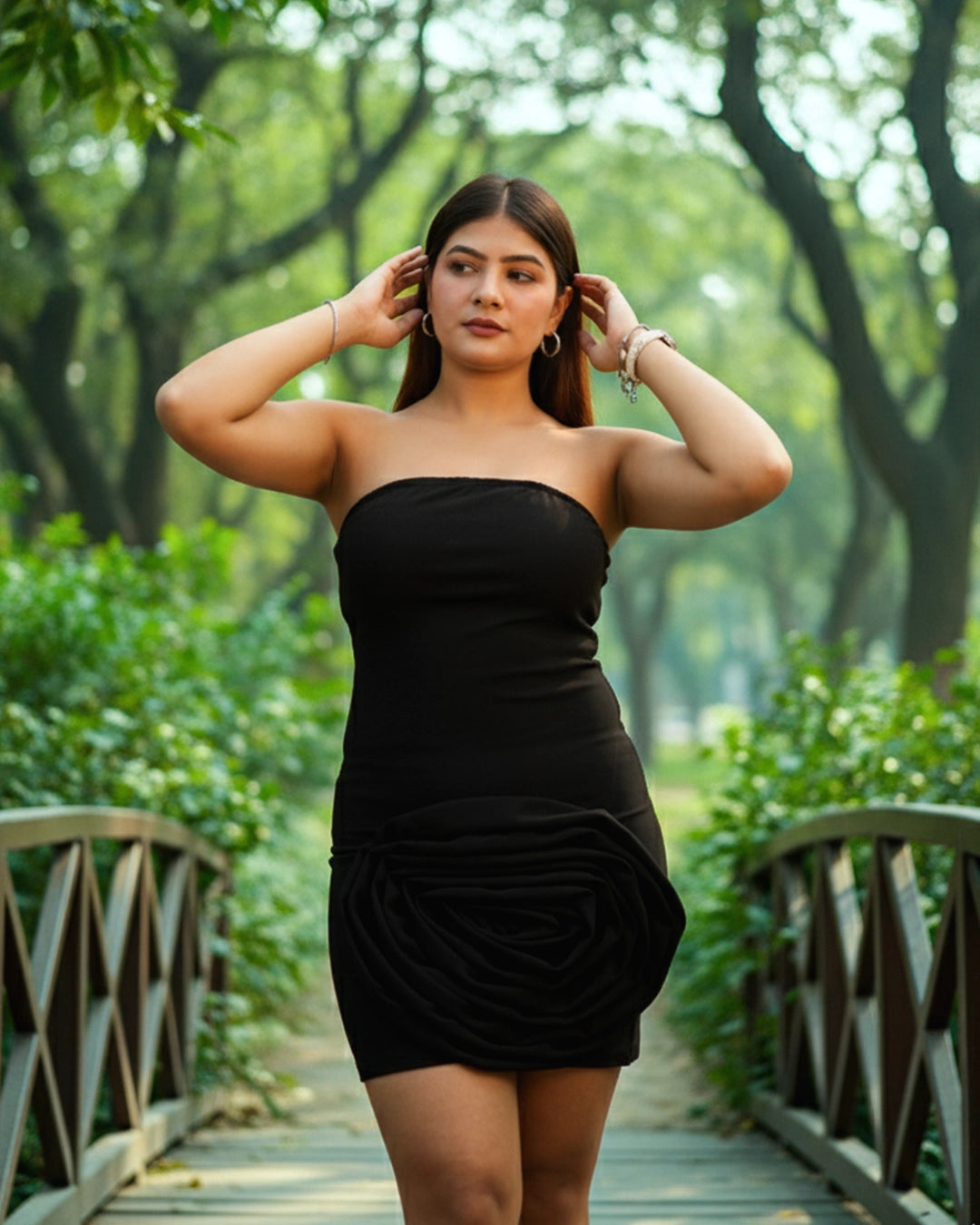 Woman in a black dress standing on a wooden bridge in a green park