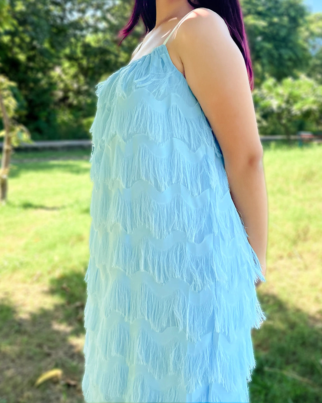 Person wearing a light blue lace dress standing outdoors with greenery in the background