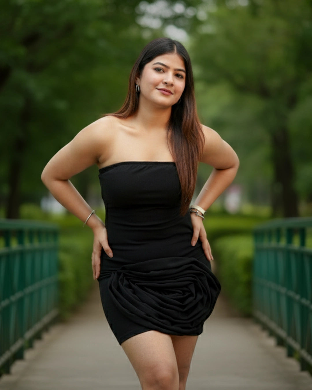 Woman in a black dress standing on a bridge with greenery in the background